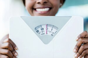 Happy woman holding a weight scale at the gym