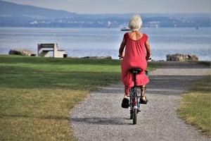 older woman riding bicycle in a park by the sea