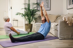 older couple stretching on yoga mats on floor of living room