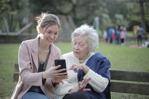 woman helping grandmother with phone in a park 