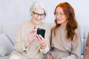 older women sitting together on the couch showing phone gossiping 