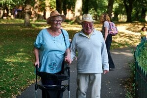 older couple walking together with walker in the park
