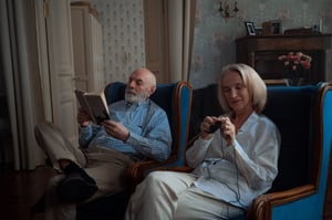 older couple sitting together inside knitting and reading 