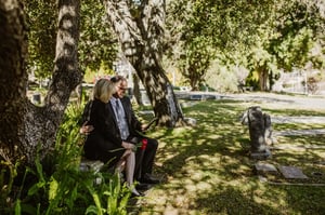 grieving older couple sitting together talking on bench