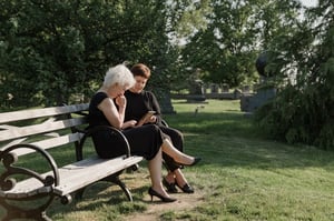 two older grieving women sitting on bench together talking 