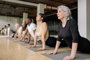senior woman participating in group exercise yoga class stretching