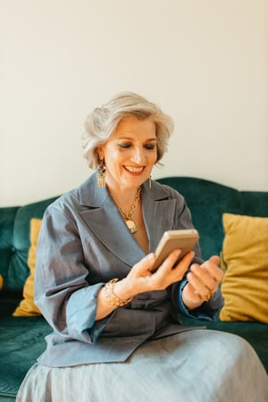 older woman smiling at her phone sitting on sofa