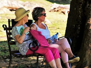 two older women sitting in the shade drinking water on hot summer day